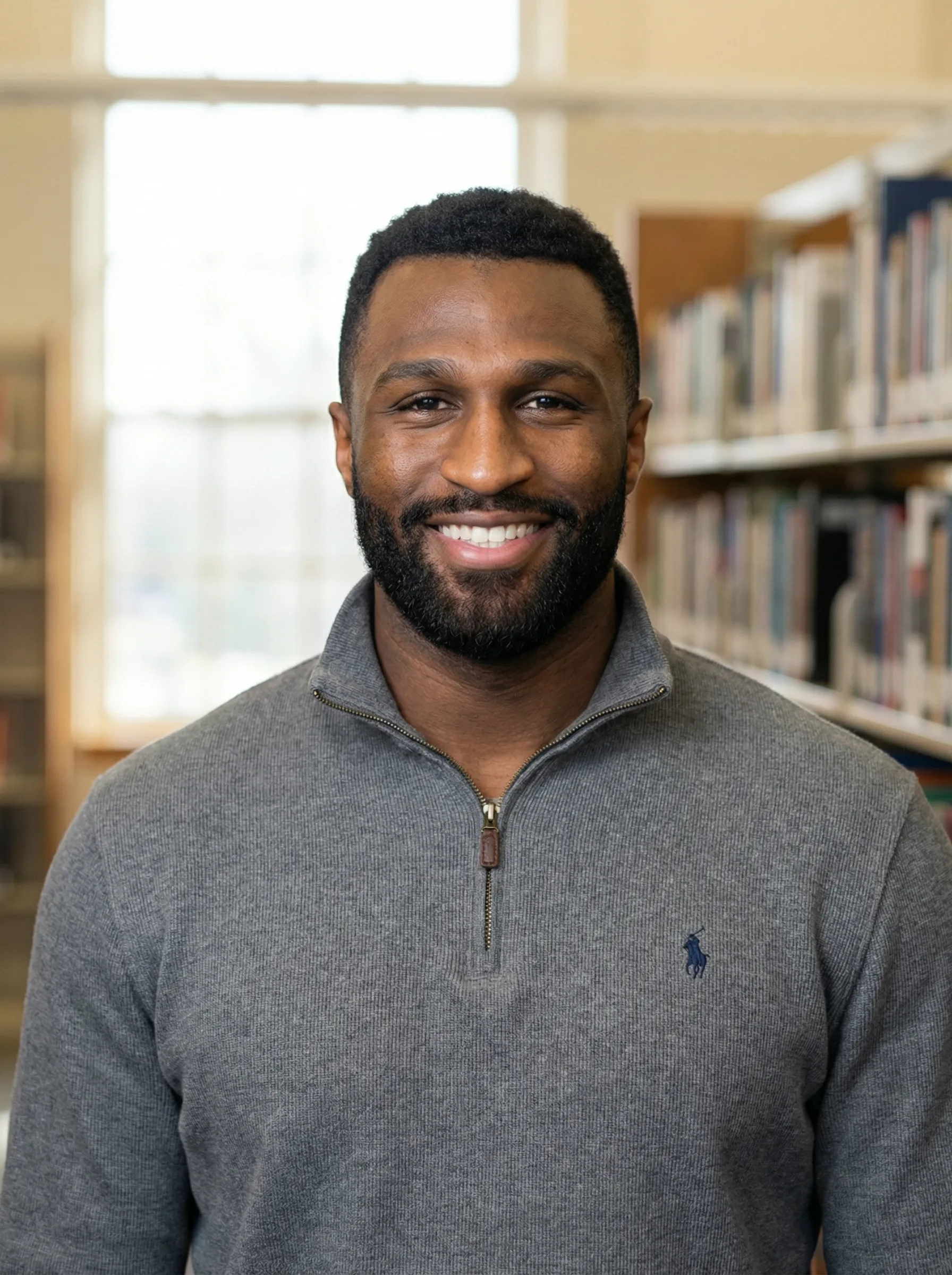 AI researcher headshot — man in a gray quarter-zip sweater in a university library